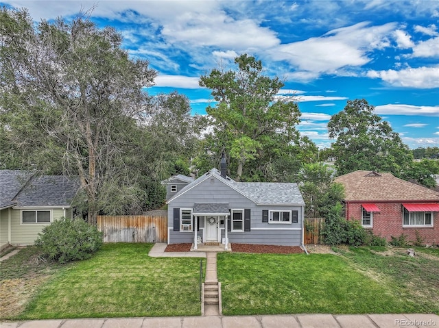 view of front of house with a front lawn, roof with shingles, and fence