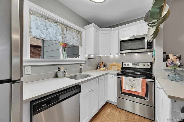 kitchen with light wood finished floors, white cabinets, stainless steel appliances, light countertops, and a sink