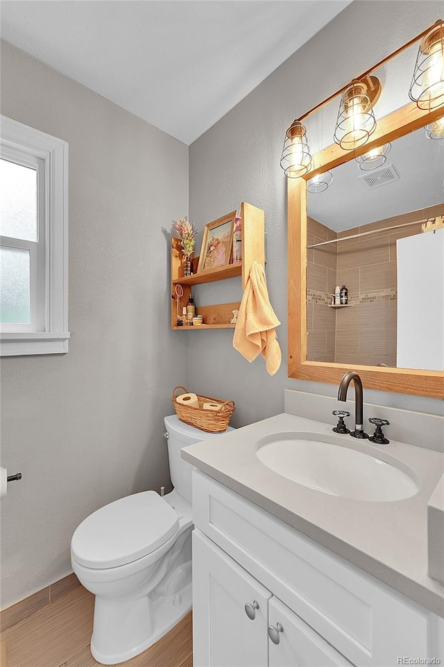 bathroom featuring toilet, a tile shower, vanity, and wood-type flooring