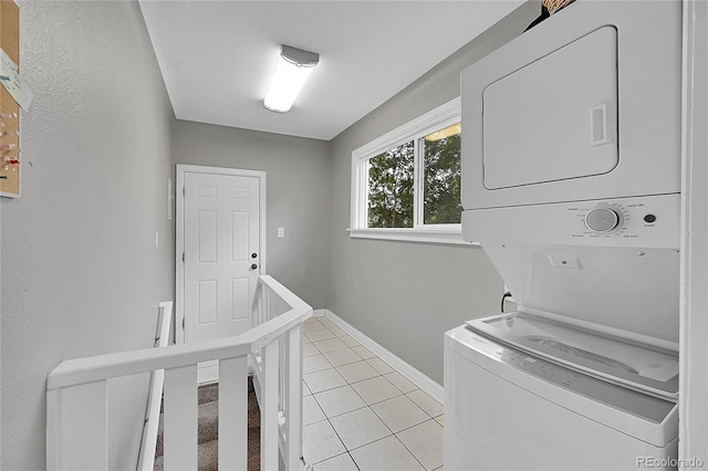 laundry room featuring stacked washer and dryer, laundry area, baseboards, and light tile patterned floors