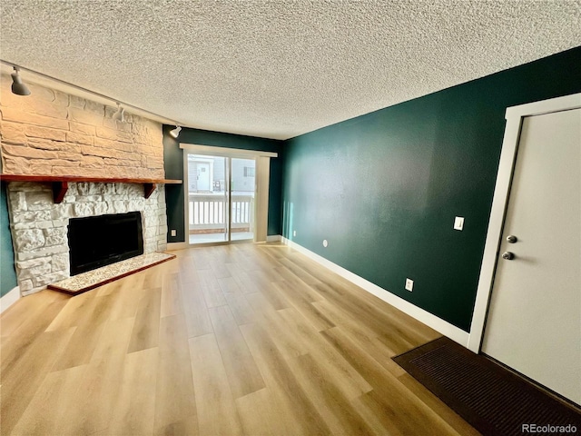 unfurnished living room featuring rail lighting, light wood-type flooring, a textured ceiling, and a stone fireplace