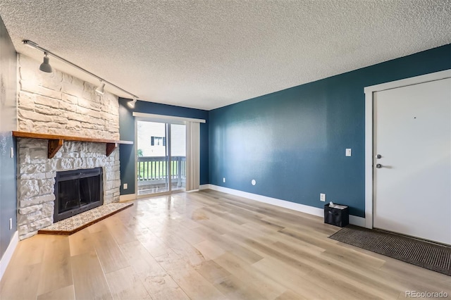 unfurnished living room featuring baseboards, track lighting, wood finished floors, and a fireplace