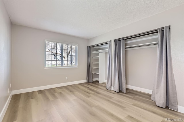unfurnished bedroom featuring baseboards, multiple closets, a textured ceiling, and light wood-style flooring