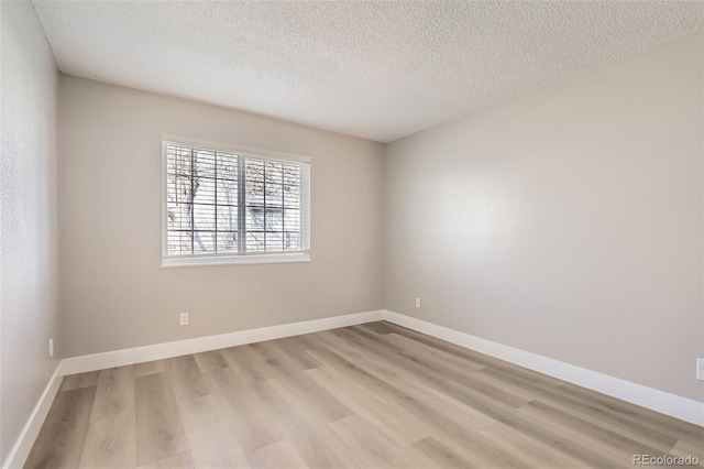 spare room with wood finished floors, a textured ceiling, and baseboards
