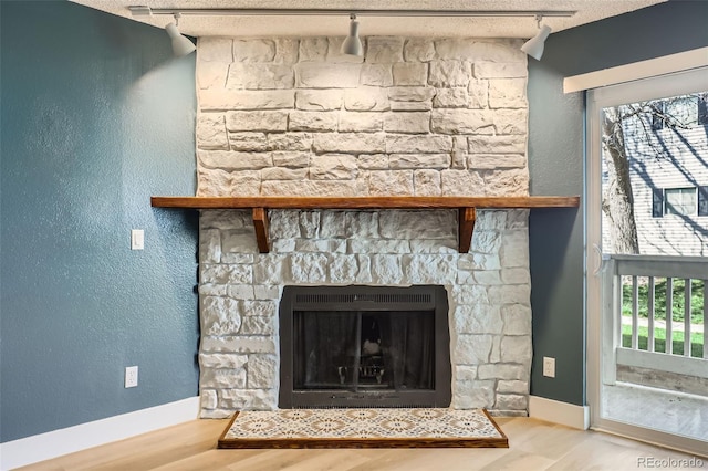 room details featuring baseboards, track lighting, wood finished floors, and a stone fireplace