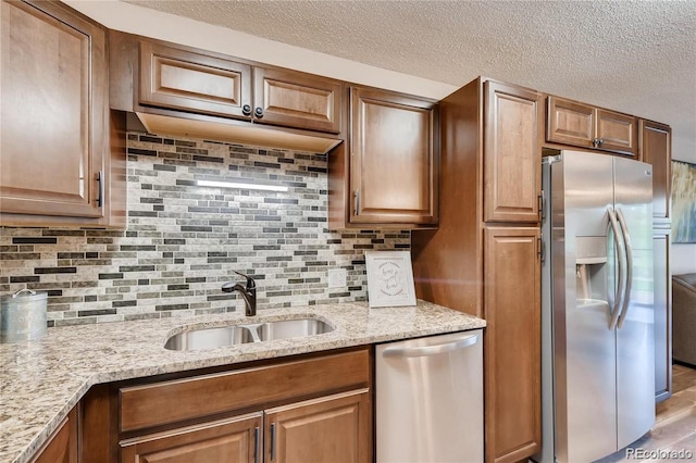 kitchen with light stone countertops, a textured ceiling, appliances with stainless steel finishes, decorative backsplash, and sink