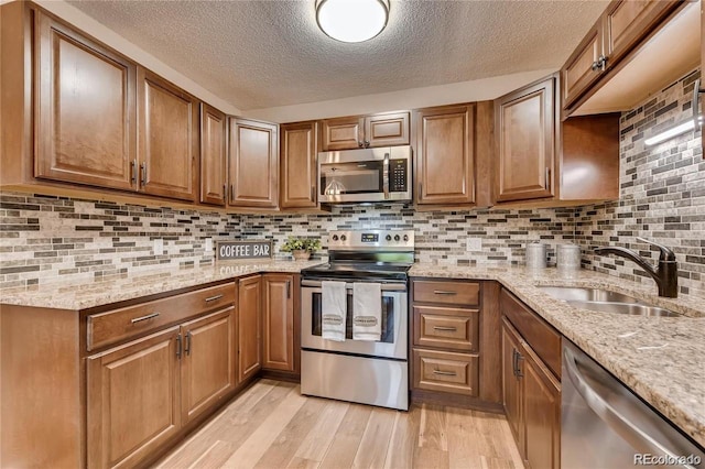 kitchen with light stone countertops, stainless steel appliances, decorative backsplash, sink, and light hardwood / wood-style flooring