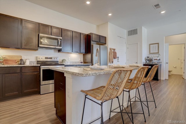 kitchen featuring light hardwood / wood-style floors, stainless steel appliances, a kitchen island with sink, a kitchen breakfast bar, and dark brown cabinets