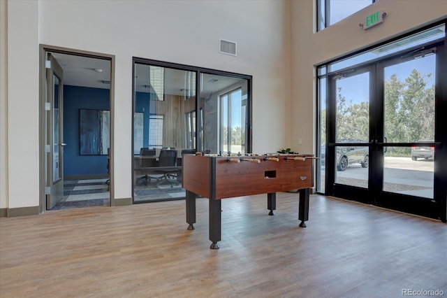 playroom with light wood-type flooring, a towering ceiling, and french doors