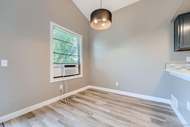 unfurnished dining area featuring cooling unit, visible vents, baseboards, vaulted ceiling, and light wood-type flooring