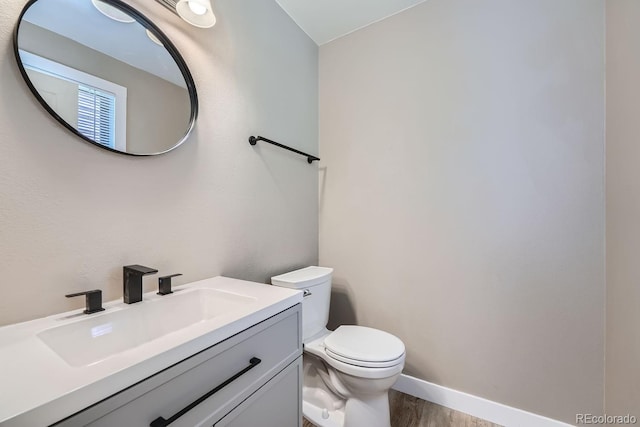 half bathroom with toilet, vanity, baseboards, and wood finished floors