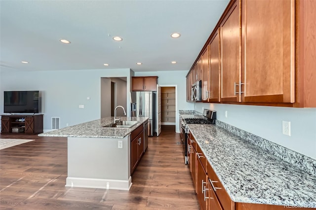 kitchen featuring dark hardwood / wood-style floors, sink, light stone counters, stainless steel appliances, and a center island with sink