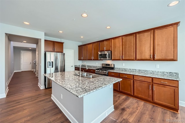 kitchen featuring sink, a kitchen island with sink, stainless steel appliances, light stone countertops, and dark hardwood / wood-style flooring