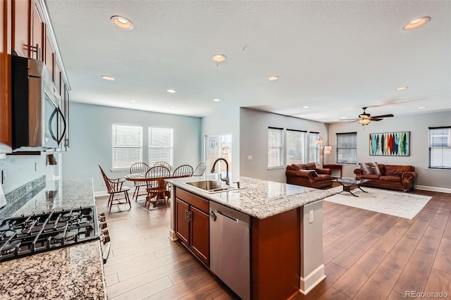 kitchen featuring dark wood-type flooring, sink, an island with sink, stainless steel appliances, and light stone countertops