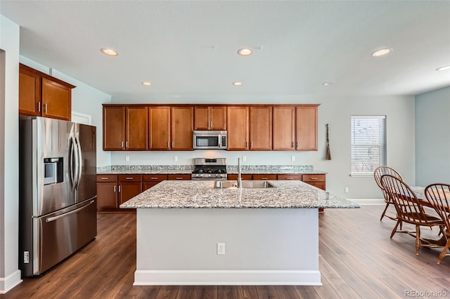 kitchen with light stone countertops, sink, stainless steel appliances, and an island with sink