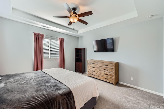 carpeted bedroom with a raised ceiling and ceiling fan