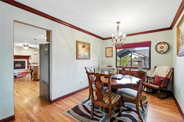 2140 S Youngfield St, Lakewood, CO 80228 - dining area featuring baseboards, a warm lit fireplace, an inviting chandelier, ornamental molding, and light wood-style flooring