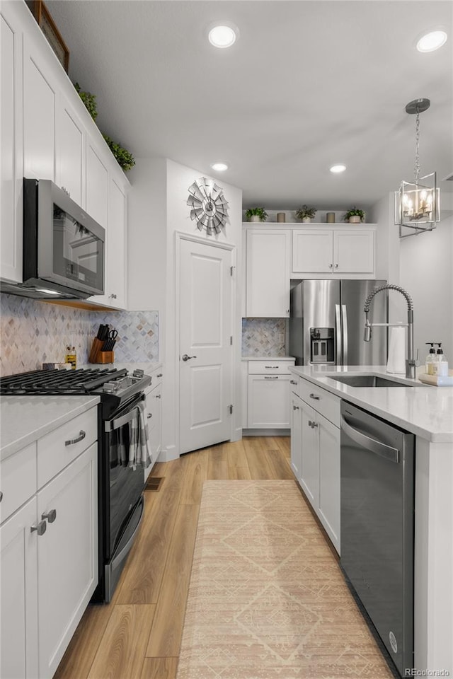 8132 Mt Harvard Rd, Littleton, CO 80125 - kitchen featuring appliances with stainless steel finishes, white cabinetry, light countertops, light wood-type flooring, and hanging light fixtures