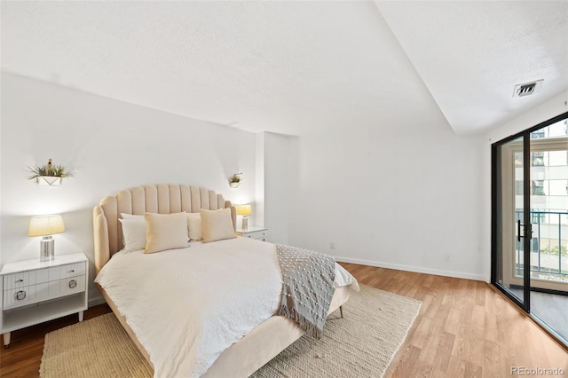 bedroom with access to exterior, light hardwood / wood-style floors, and a textured ceiling