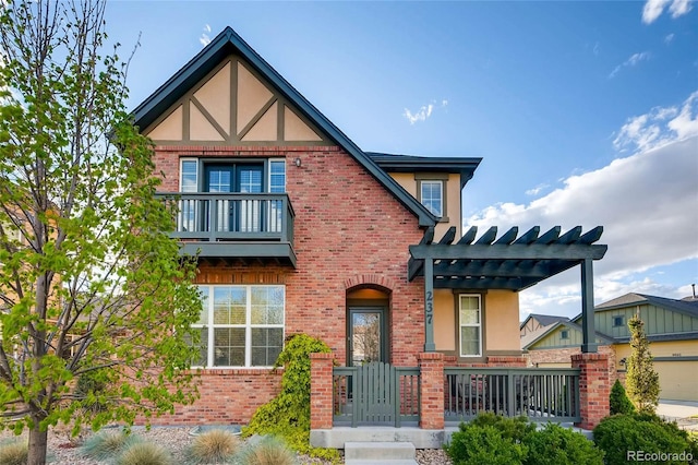 tudor house featuring a pergola, brick siding, a balcony, and stucco siding