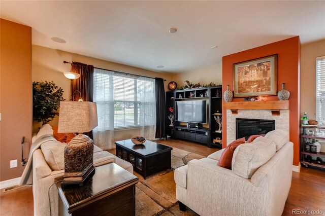 living area featuring visible vents, a glass covered fireplace, baseboards, and wood finished floors