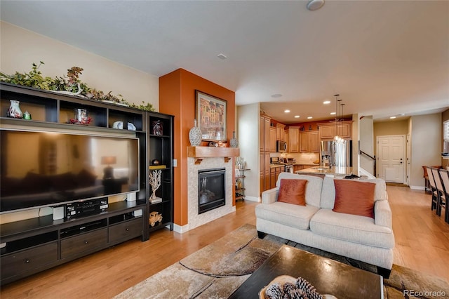 living area with recessed lighting, light wood-style floors, a glass covered fireplace, and baseboards