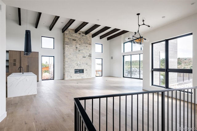 unfurnished living room featuring beam ceiling, light hardwood / wood-style floors, a chandelier, a fireplace, and high vaulted ceiling