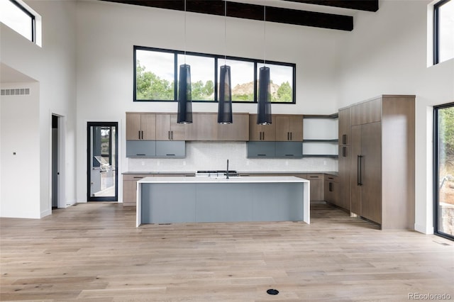 kitchen with light hardwood / wood-style flooring, an island with sink, a towering ceiling, and hanging light fixtures