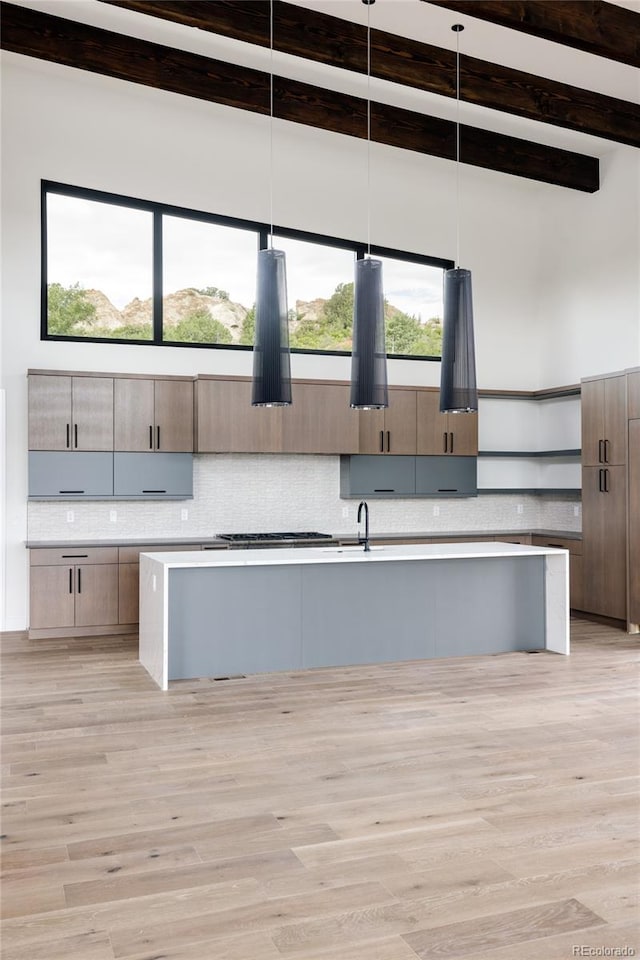 kitchen with hanging light fixtures, beamed ceiling, light hardwood / wood-style floors, and an island with sink