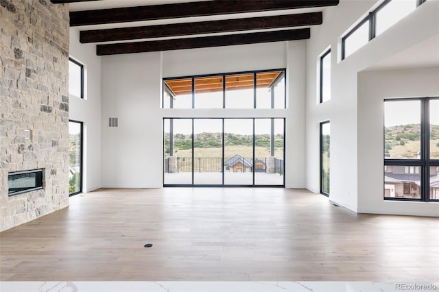 unfurnished living room featuring a high ceiling, a healthy amount of sunlight, a stone fireplace, and hardwood / wood-style flooring