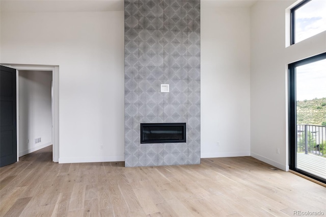 unfurnished living room with a towering ceiling, a fireplace, and light hardwood / wood-style flooring