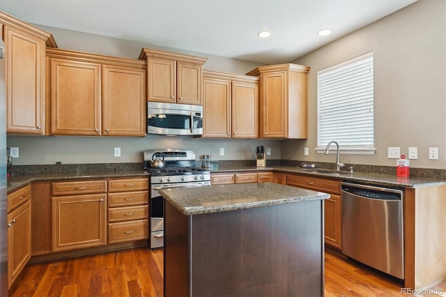 kitchen with appliances with stainless steel finishes, a sink, wood finished floors, a center island, and recessed lighting