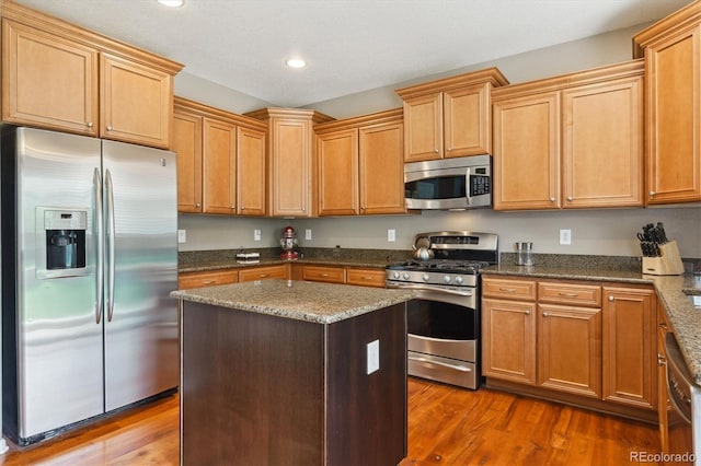 kitchen featuring stainless steel appliances, wood finished floors, recessed lighting, dark stone countertops, and a center island