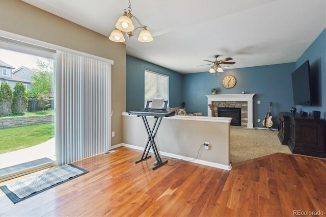 living area featuring plenty of natural light, a ceiling fan, wood finished floors, and a stone fireplace