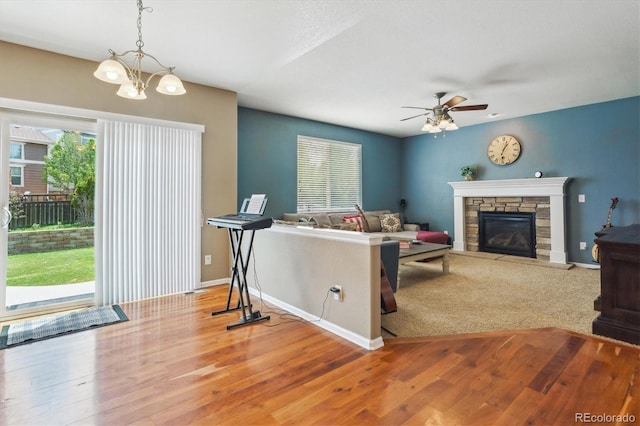 living room featuring ceiling fan, a fireplace, wood finished floors, baseboards, and a chandelier
