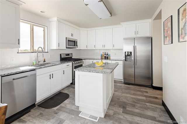 kitchen featuring stainless steel appliances, a sink, decorative backsplash, white cabinetry, and light stone counters