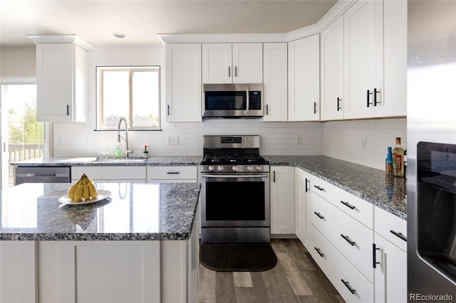 kitchen featuring stainless steel appliances, a sink, wood finished floors, decorative backsplash, and white cabinets