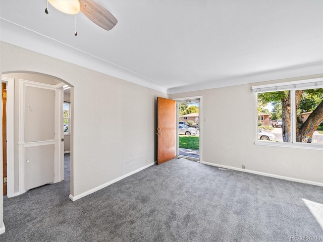 spare room featuring baseboards, carpet flooring, visible vents, ceiling fan, and arched walkways