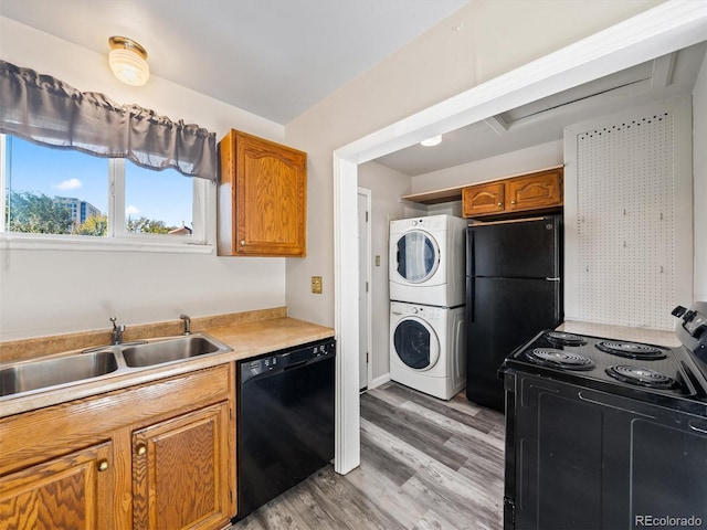kitchen featuring brown cabinetry, black appliances, stacked washer and clothes dryer, light wood-style flooring, and light countertops