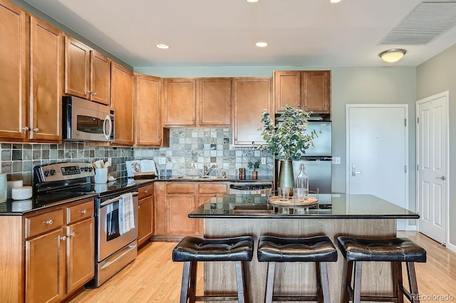 kitchen featuring light hardwood / wood-style flooring, backsplash, stainless steel appliances, a center island, and a kitchen bar