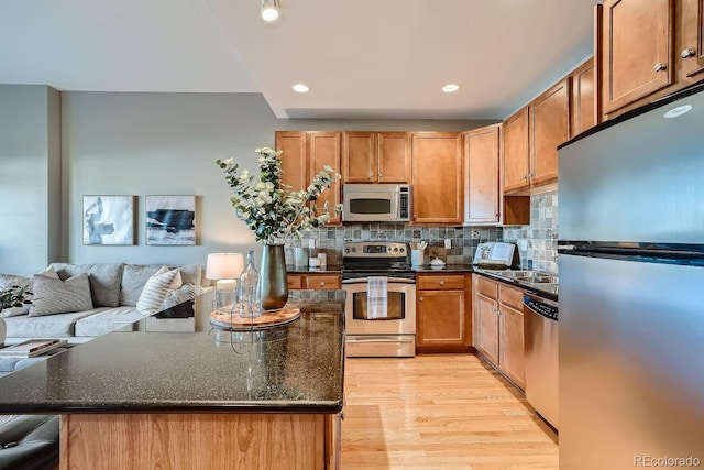 kitchen featuring dark stone countertops, backsplash, light wood-type flooring, and appliances with stainless steel finishes