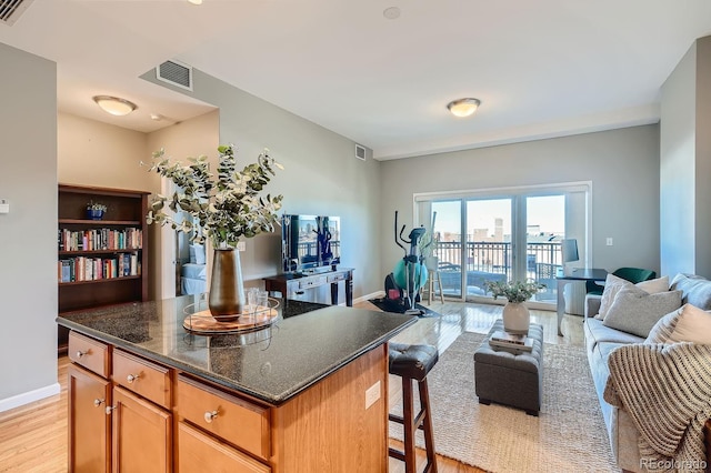 kitchen featuring dark stone counters, a kitchen breakfast bar, a center island, and light hardwood / wood-style flooring