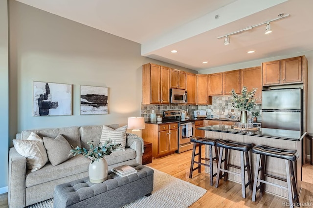 kitchen with track lighting, a kitchen breakfast bar, stainless steel appliances, light hardwood / wood-style floors, and backsplash