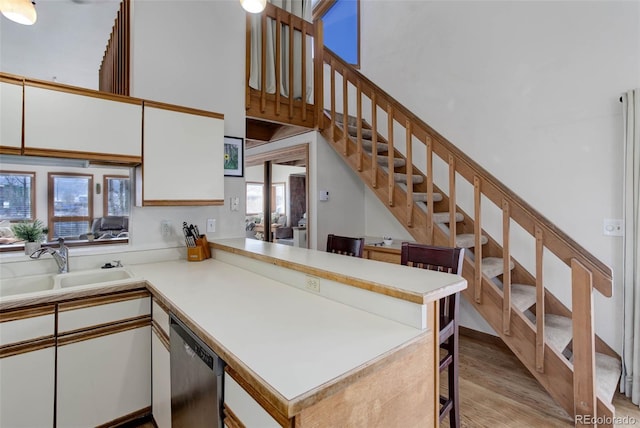 kitchen with kitchen peninsula, light wood-type flooring, stainless steel dishwasher, sink, and white cabinetry