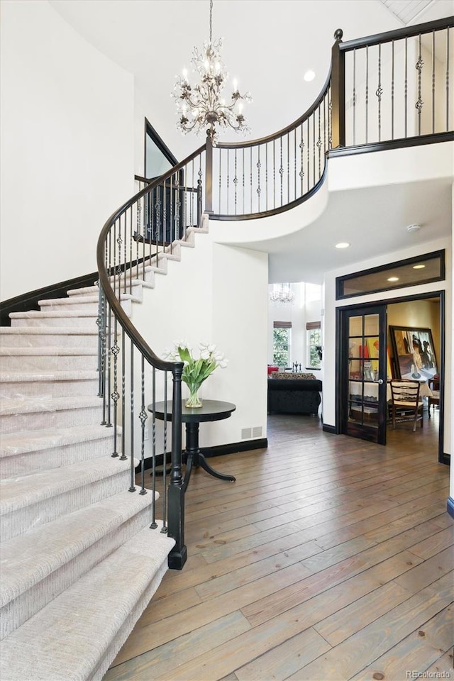 stairs with hardwood / wood-style floors, a towering ceiling, and a chandelier