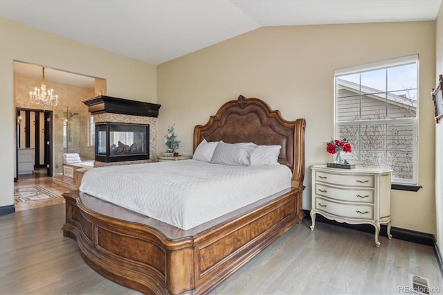 bedroom featuring lofted ceiling, a multi sided fireplace, wood-type flooring, and a chandelier