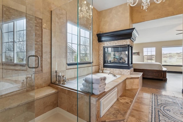 bathroom featuring tile patterned floors, tile walls, a notable chandelier, a multi sided fireplace, and shower with separate bathtub