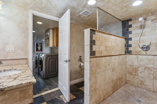 bathroom with washer and dryer, a tile shower, and vanity