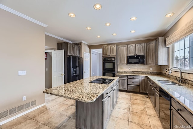 kitchen with sink, a kitchen island, light stone counters, light tile patterned flooring, and black appliances