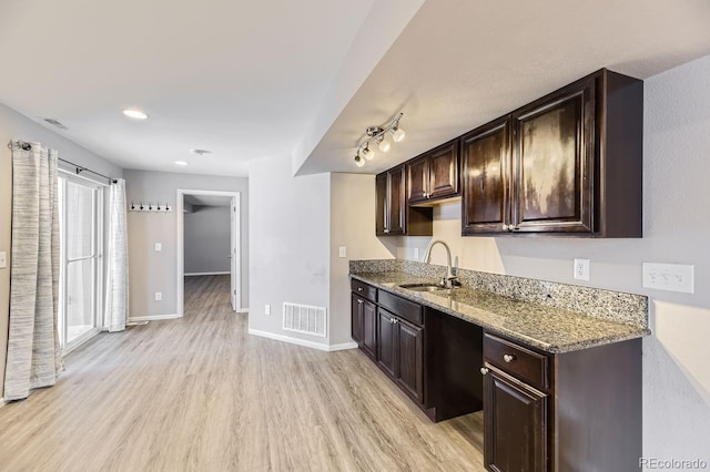 kitchen with dark brown cabinetry, stone counters, sink, and light hardwood / wood-style floors